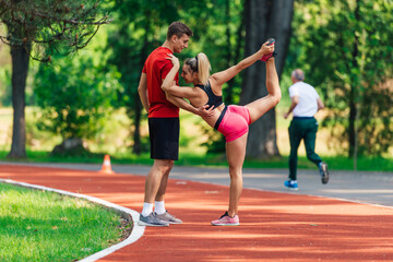 Young male athlete supporting his young female partner while she is stretching her legs after running on a race track.