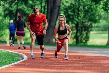 Fototapeta premium Young couple stretching before starting their morning jogging routine on a tartan track at the park.