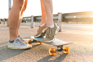 Girl standing on a longboard beside her boyfriend on street at sunset