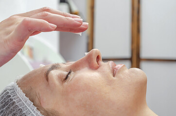 Beautician hand applies cream on face of woman in a spa salon.