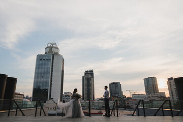 Fototapeta premium Romantic and happy caucasian couple in wedding clothes walking and hugging at the city streets. Love, relationships, romance, happiness, urban concept. Bride and groom celebrate their marriage.