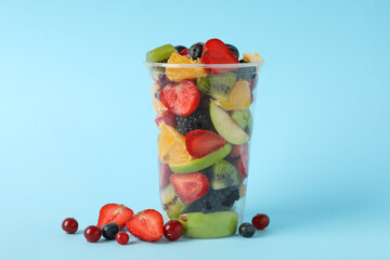 Fruit salad in takeaway cup on blue background, space for text