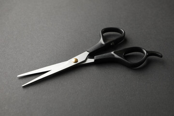 Black hairdresser scissors on black background, space for text