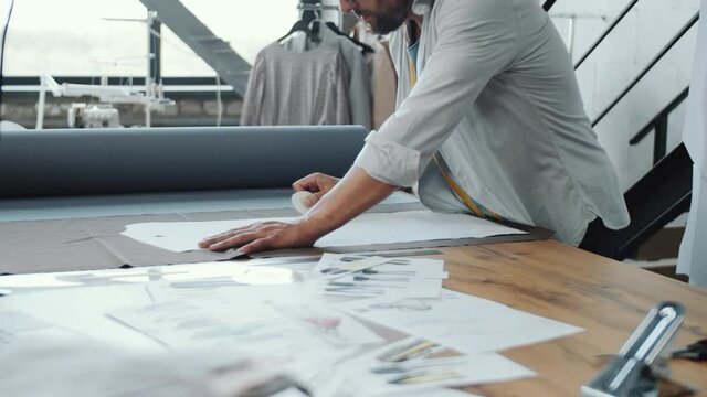 Professional male tailor drawing contour of sewing pattern with chalk on fabric while working in dressmaking studio