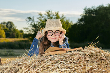 Naklejka na ściany i meble Reading girl sits over the haystack roll on field in countryside. High quality photo