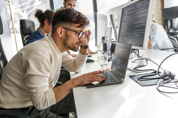 Young programmer sitting at the desk in his office and working on new code.