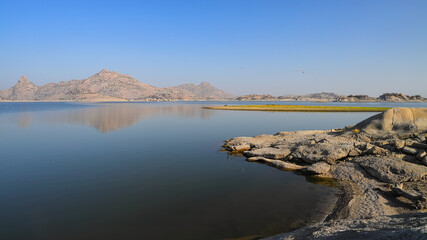 Fototapeta na wymiar An image of landscape of Jawai dam with clear blue sky and Aravalli mountain ranges with its reflection in water at Jawai in Rajasthan India