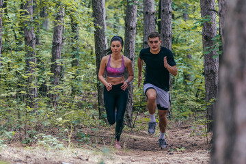 Young athletic couple is running outdoors in the wooded forest area