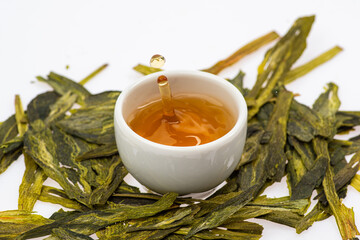 loose green tea next to a cup of tea on a white background