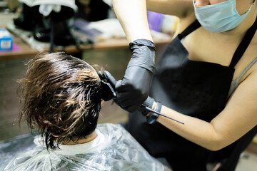 Hairdresser dyes woman hair. Hairdresser colorist dyes the hair of woman. Beautician, hand. Hairdressing during the coronavirus