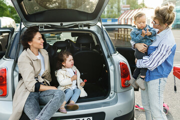 Happy women and their beautiful kids beside a car on a parking lot