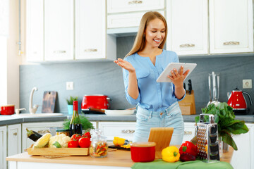 Young beautiful caucasian woman cooking and using her digital tablet in kitchen