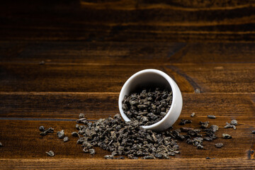loose black tea next to a cup of tea on a dark wooden background