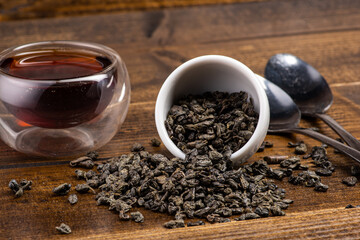 loose black tea next to a cup of tea on a dark wooden background