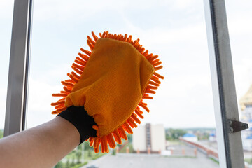 Washing the windows of the glass balcony with a hand mitt. A window-cleaning glove is worn on a man's hand.