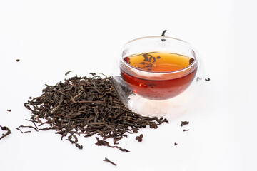 loose black tea next to a cup of tea on a white background