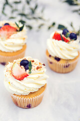 Tasty cupcakes decorated with cream cheese, blueberry and strawberry. Sweet baked pastry. Holidays cupcakes with fruit.