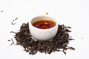loose black tea next to a cup of tea on a white background