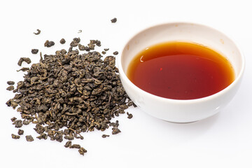 loose black tea next to a cup of tea on a white background