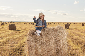 Reading girl sits over the haystack roll on field in countryside. High quality photo