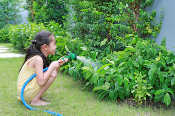 Asian little child girl pouring water spray on trees. Kid watering plants in the garden near his...