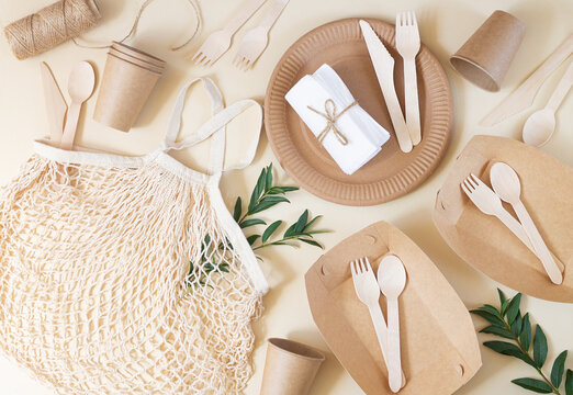 Zero waste, plastic-free and eco-friendly living. Paper disposable tableware, wooden cutlery and cotton mesh bag top view on beige table