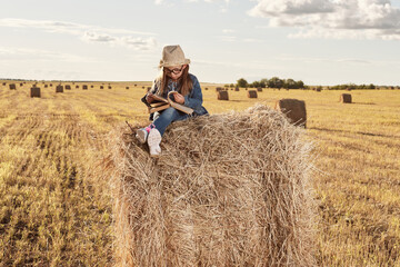 Reading girl sits over the haystack roll on field in countryside. High quality photo