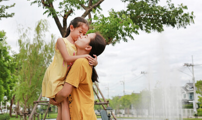 Portrait of asian mother and daughter relaxing in park. Mum carrying her child girl in public garden