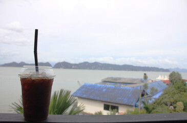 Americano black coffee packed in a clear glass placed on a red wooden floor with a natural background of the sea and mountains.