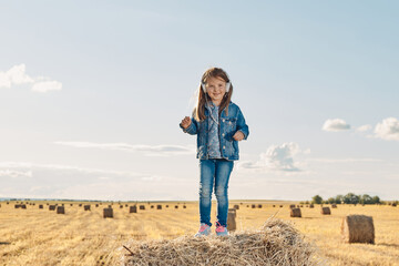Naklejka na ściany i meble A cute little girl listens to music and dances on a haystack. High quality photo