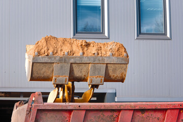 Excavator loads dump truck soil on construction site. Backhoe dumping sand in tipper. Wheel loader loads sand into heavy mining dump truck. Digging and excavation operations