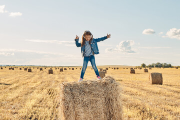 A cute little girl listens to music and dances on a haystack. High quality photo