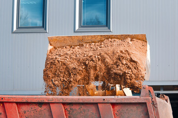 Excavator loads dump truck soil on construction site. Backhoe dumping sand in tipper. Wheel loader loads sand into heavy mining dump truck. Digging and excavation operations.