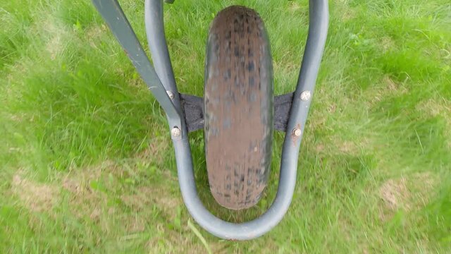 Work In The Field Concept. Close-up View Of A Wheelbarrow Wheel Plan, Top View. Farmer Pushing A Wheelbarrow In A Green Meadow, Backyard.