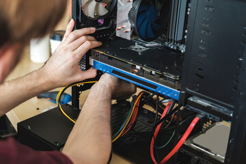 Young man repairs a computer system unit, changes parts, video card and hard drive, sets new...
