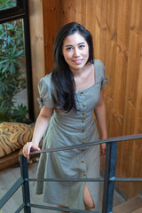 The young beautiful girl is standing by the window and looks out of the window in the morning. Portrait of a happy young girl standing by window at home. Relax woman smiling happily over glass window.