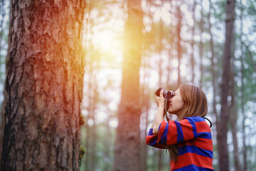 An Asian woman in a red dress holding a camera with a pine forest in the background
