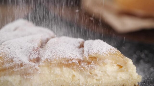 Closeup powdered sugar falling down on piece of delicious sweet apple pie on table in kitchen