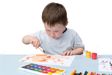 a small boy sits at a table and draws with paints. The child is engaged, does not look into the frame. horizontal photo, soft focus.