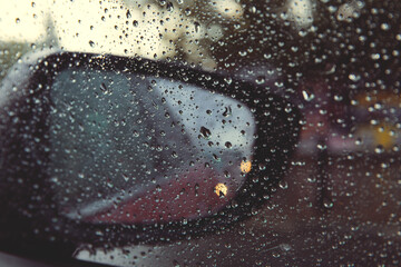 Rear view mirror seen through rain drops on the car window.