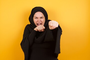 Portrait of strong and determined Middle aged muslim woman wearing black hijab over yellow...