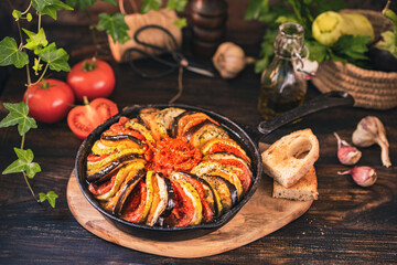 Ratatouille made of zucchini, eggplants, peppers, onions, garlic and tomatoes slices with aromatic herbs, bread. Rustic wooden table. Traditional French food, vegetable, vegan healthy dish. Copy space