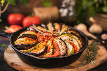 Ratatouille made of zucchini, eggplants, peppers, onions, garlic and tomatoes slices with aromatic herbs, bread. Rustic wooden table. Traditional French food, vegetable, vegan healthy dish. Copy space