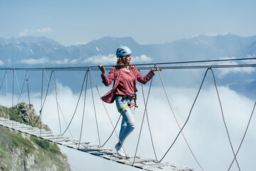 Wanderlust and adventures. .Extreme vacation. A woman walks on a suspension bridge high in the mountains at the level of a cloud.
