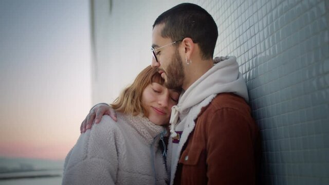 Cute ginger young girl in love leaning on boyfriend tenderly hugging sea side sunrise view, charming Hispanic affectionate couple in jackets enjoying moment positive feeling togetherness embrace