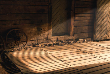 Wooden wheel leaned against a wooden wall with light streaming inside the room from opened doors.