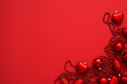 Christmas tree decorations on the red background with copy space. Red baubles and beads. New year flat lay.