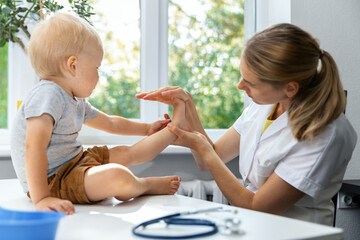 female orthopedist examining little child foot condition in clinic - obrazy, fototapety, plakaty