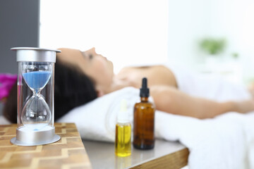 Woman lies in spa salon next to an hourglass and aromatic oils. Spa services concept