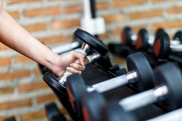 Naklejka na ściany i meble Closeup a man's hand holds a dumbbell with his right hand in the gym.